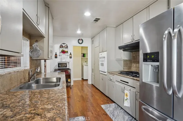 a kitchen with granite countertop a refrigerator a sink dishwasher stove top oven and refrigerator