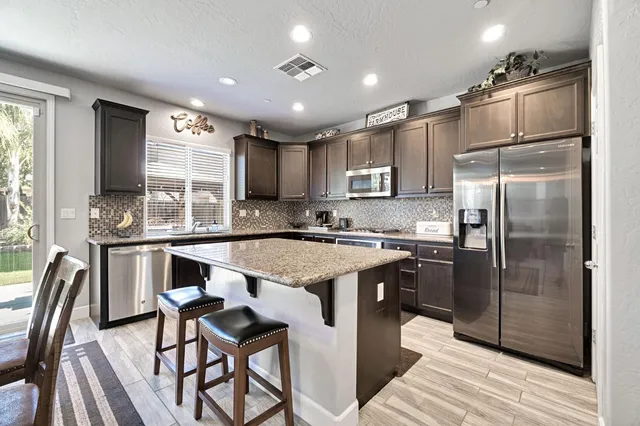 a modern kitchen with stainless steel appliances granite countertop a refrigerator a sink a stove a dining table and chairs