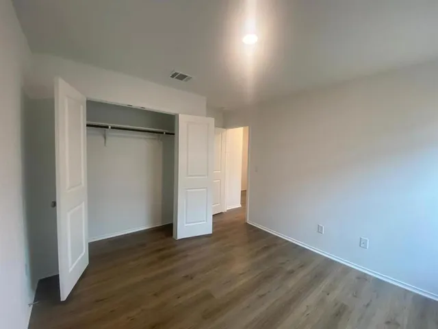 a view of an empty room with wooden floor and closet
