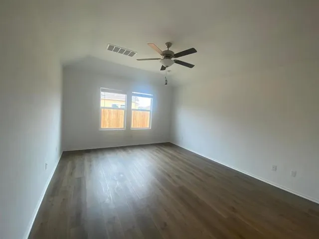 an empty room with wooden floor fan and windows