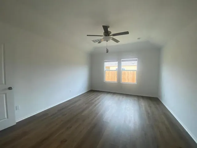 an empty room with wooden floor fan and windows