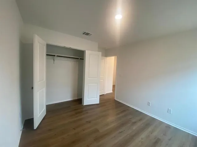 a view of an empty room with wooden floor & closet