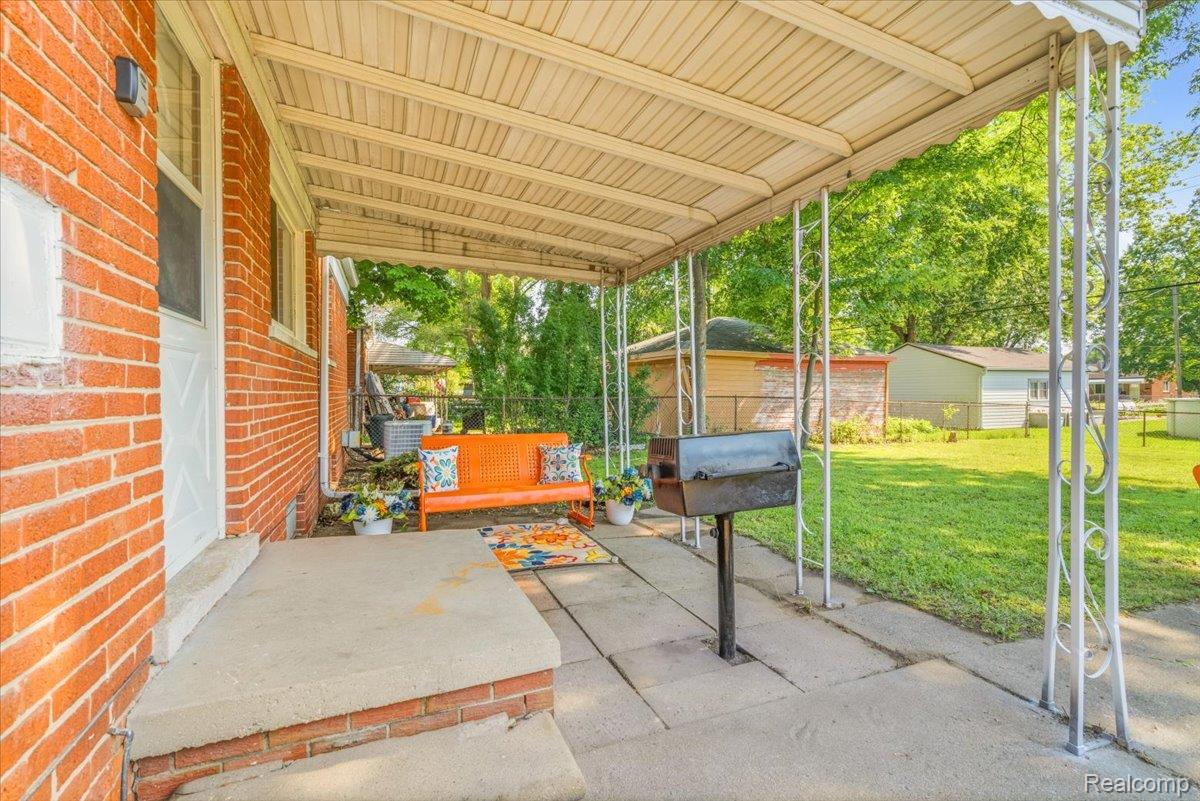 11802 Columbia Street Redford, MI 48239 - Photo 35 of 39 Covered concrete patio featuring a white aluminum awning supported by decorative posts, a red brick exterior wall, and a concrete patio surface