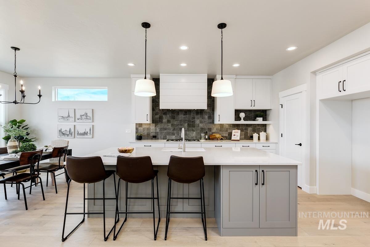 992 East Crescendo Street Meridian, ID 83642 - Photo 12 of 38 Dual tone kitchen featuring light wood-style flooring, a kitchen breakfast bar, two tone cabinetry, an island with sink, and light stone counters