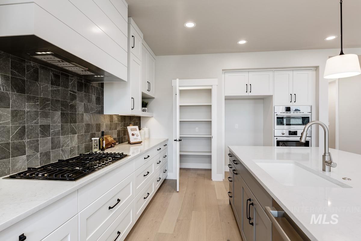 992 East Crescendo Street Meridian, ID 83642 - Photo 13 of 38 Two tone kitchen with light wood-type flooring, light stone countertops, hanging light fixtures, two tone color scheme, and stainless steel appliances