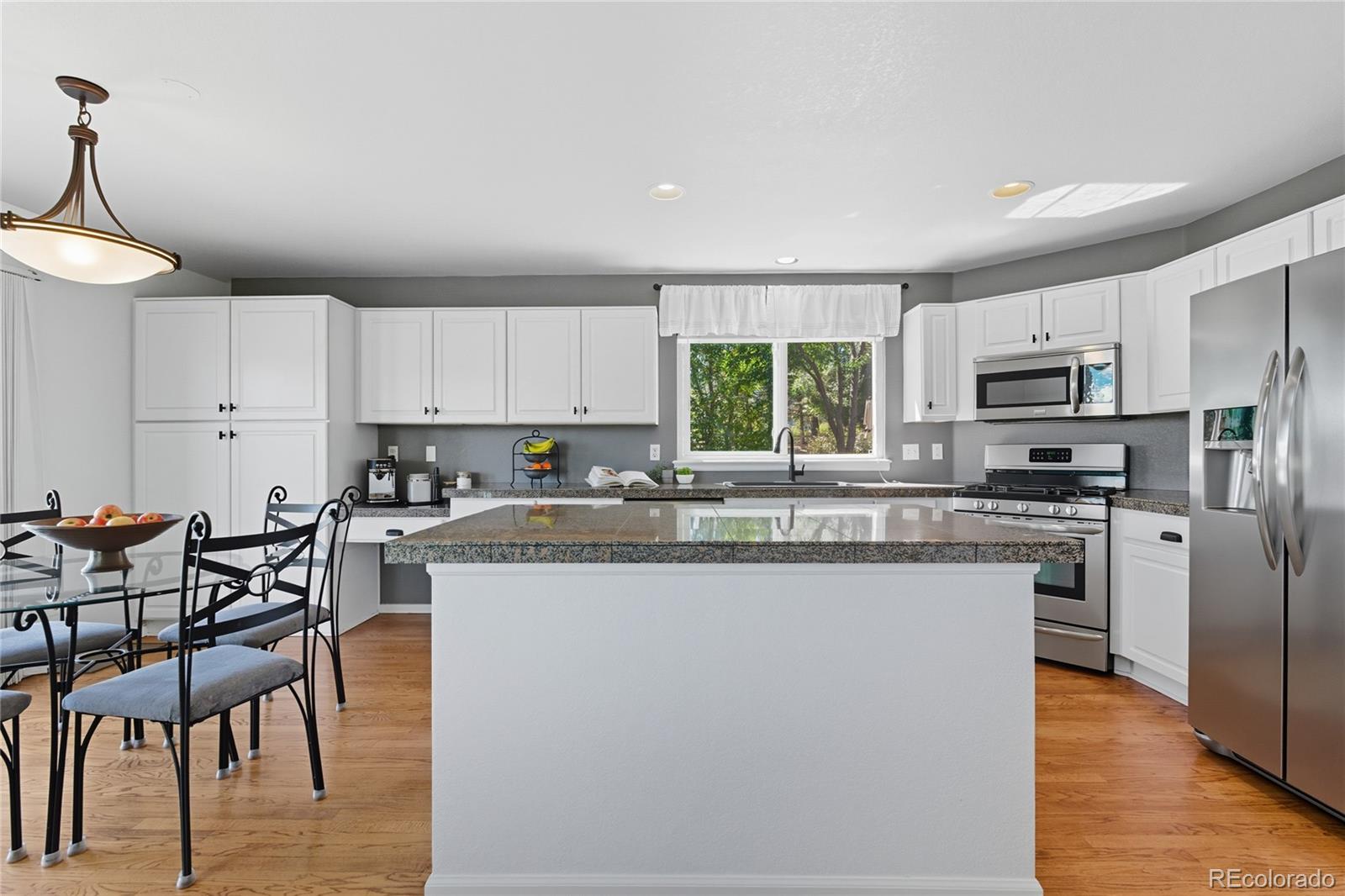 5126 Tuscany Court Highlands Ranch, CO 80130 - Photo 9 of 50 a kitchen with stainless steel appliances granite countertop a stove top oven a refrigerator a sink and a dining table with wooden floor