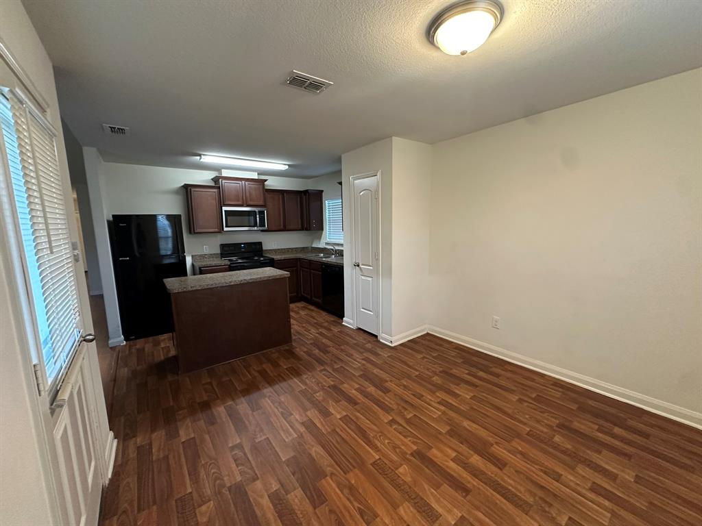 1818 Clegg Street Howe, TX 75459 - Photo 24 of 34 Kitchen and dining area featuring wood-finish flooring, dark wood cabinetry, granite-style countertops, and a full suite of black appliances