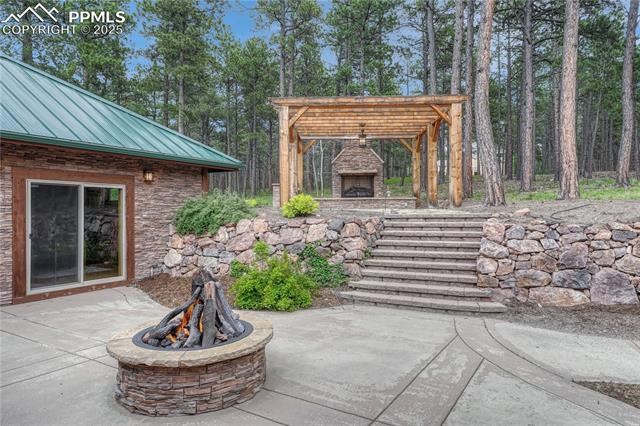 15975 Winding Trail Road Colorado Springs, CO 80908 - Photo 42 of 50 Stone stairs lead to a pergola with an outdoor grill and gas log fireplace
