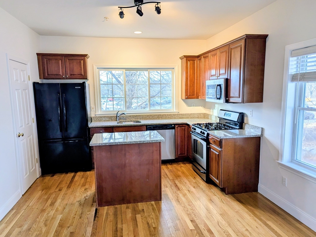 19 Railroad Street, Unit D2 Acton, MA 01720 - Photo 3 of 13 a kitchen with stainless steel appliances granite countertop a refrigerator a sink dishwasher a stove with wooden floor and cabinets next to a window