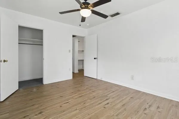 an empty room with wooden floor ceiling fan and windows