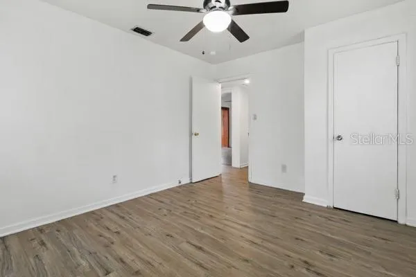an empty room with wooden floor ceiling fan and window