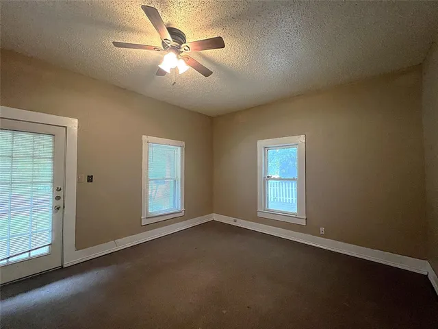 an empty room with chandelier fan and windows