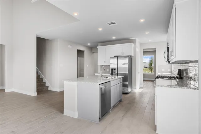 a kitchen with stainless steel appliances kitchen island granite countertop a refrigerator oven a sink dishwasher and white cabinets with wooden floor