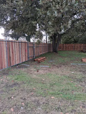 a view of a backyard with large trees and wooden fence