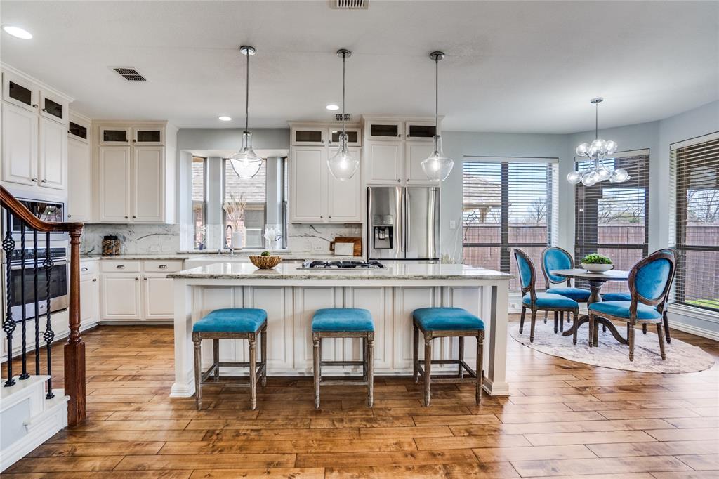 1804 Goodnight Lane Allen, TX 75002 - Photo 17 of 35 Kitchen featuring light stone counters, a center island, stainless steel appliances, light wood-type flooring, and a chandelier