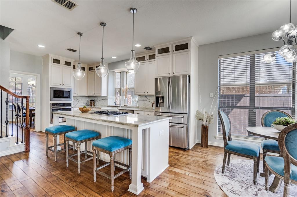 1804 Goodnight Lane Allen, TX 75002 - Photo 18 of 35 Kitchen with stainless steel appliances, a kitchen island, light stone countertops, white cabinetry, and a kitchen bar