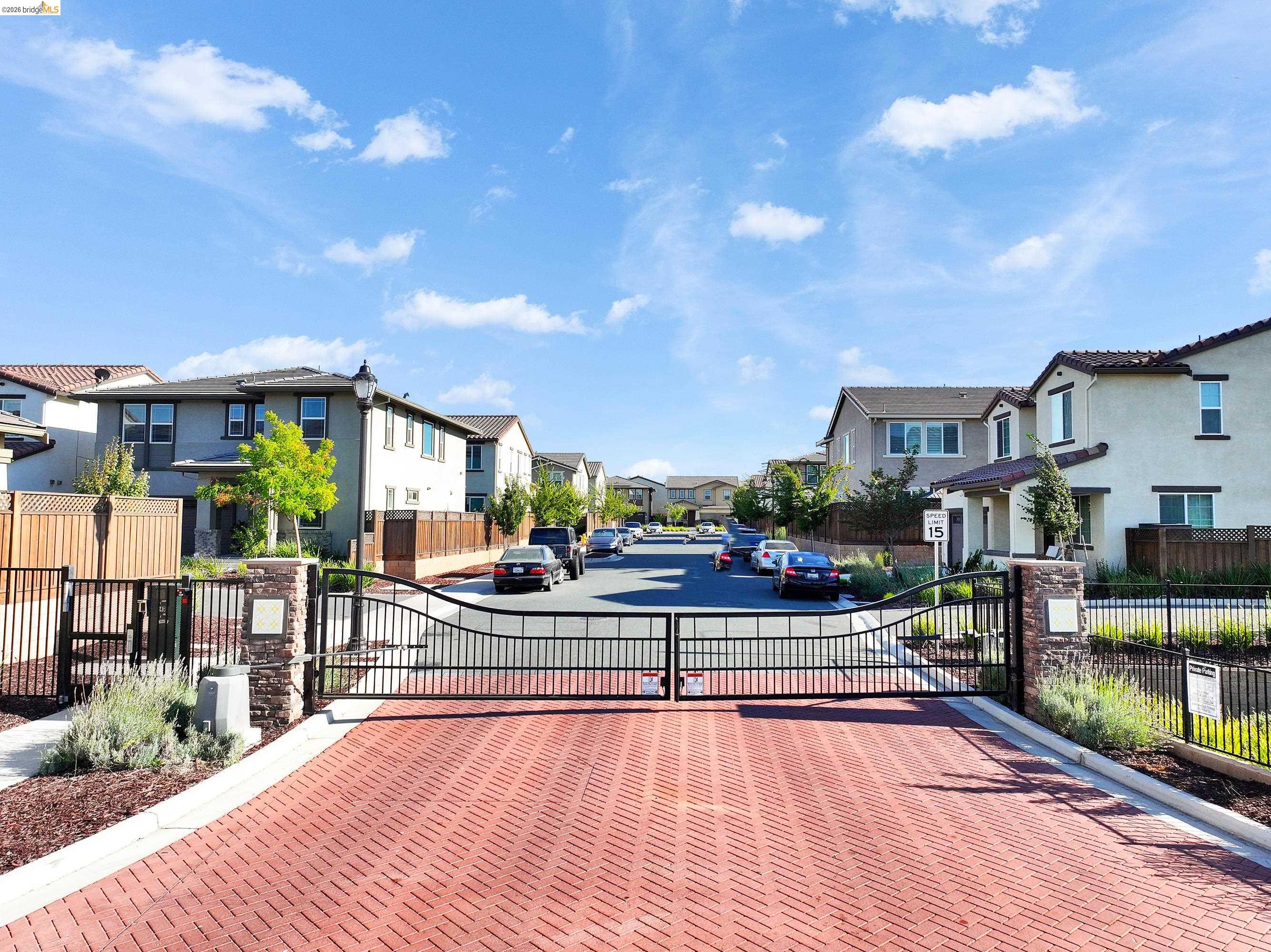 Community entrance featuring paver driveway, wrought iron gates, and stone pillars
