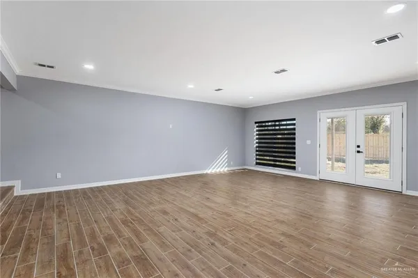a view of an empty room with wooden floor and windows