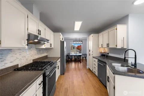 a kitchen with stainless steel appliances granite countertop a stove top oven a sink a dining table and chairs with wooden floor