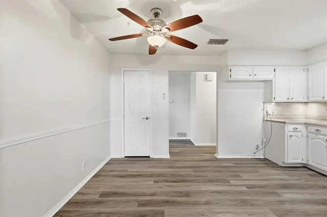 a view of an empty room and kitchen with wooden floor