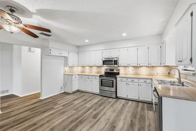 a kitchen with stainless steel appliances a sink dishwasher stove refrigerator and white cabinets with wooden floor