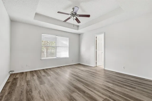 an empty room with wooden floor ceiling fan and windows