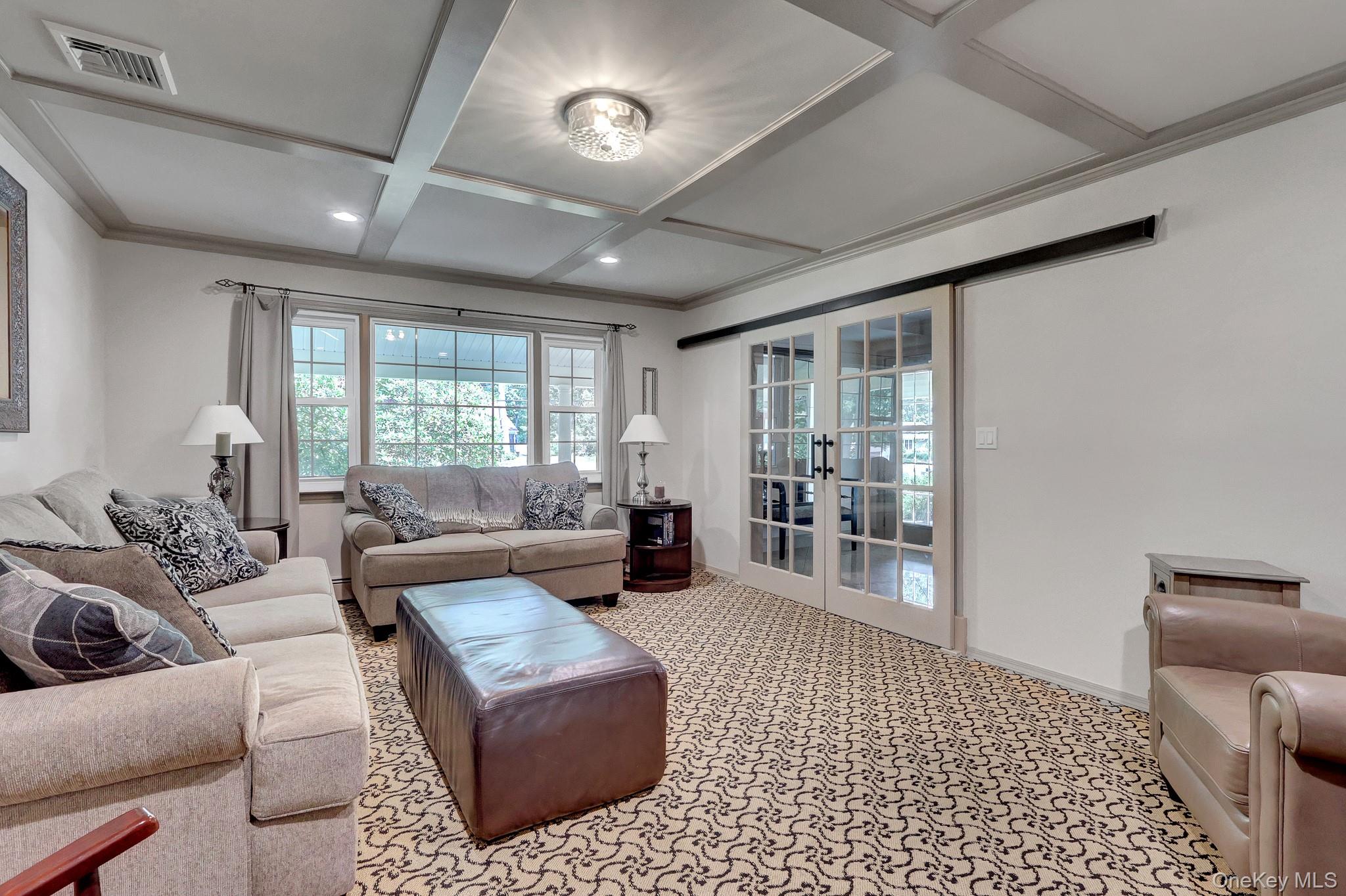 24 Fox Road East Setauket, NY 11733 - Photo 18 of 48 Living area featuring a coffered ceiling with recessed lighting and a central flush-mount fixture, patterned carpet flooring, a large window array with outdoor views, and glass-paned double doors on a barn door track, hidden hard wood floors