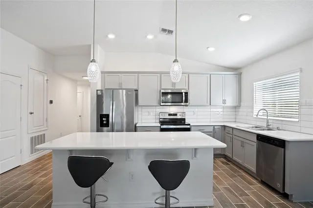 a kitchen with stainless steel appliances a stove a sink a microwave a refrigerator and white cabinets with wooden floor