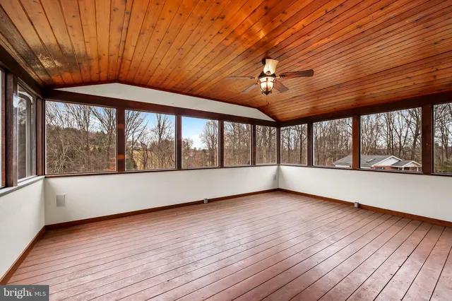 a big room with wooden floor a ceiling fan and windows