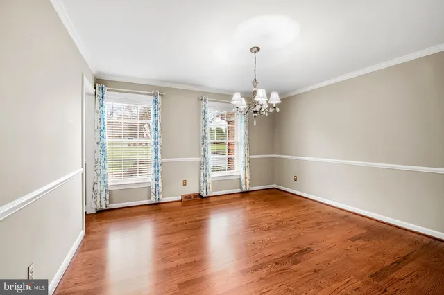 an empty room with wooden floor chandelier and windows