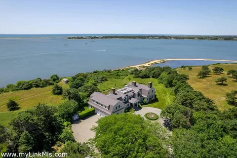 an aerial view of ocean with residential house with outdoor space and trees in the background