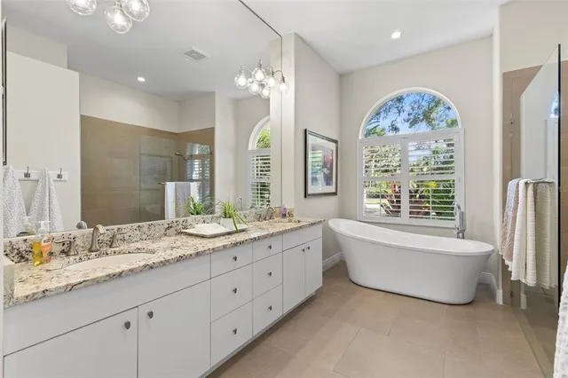 a bathroom with a granite countertop double vanity sink a large mirror a bathtub and next to a window
