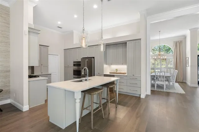 a kitchen with kitchen island a stove a refrigerator a sink a dining table and chairs with wooden floor