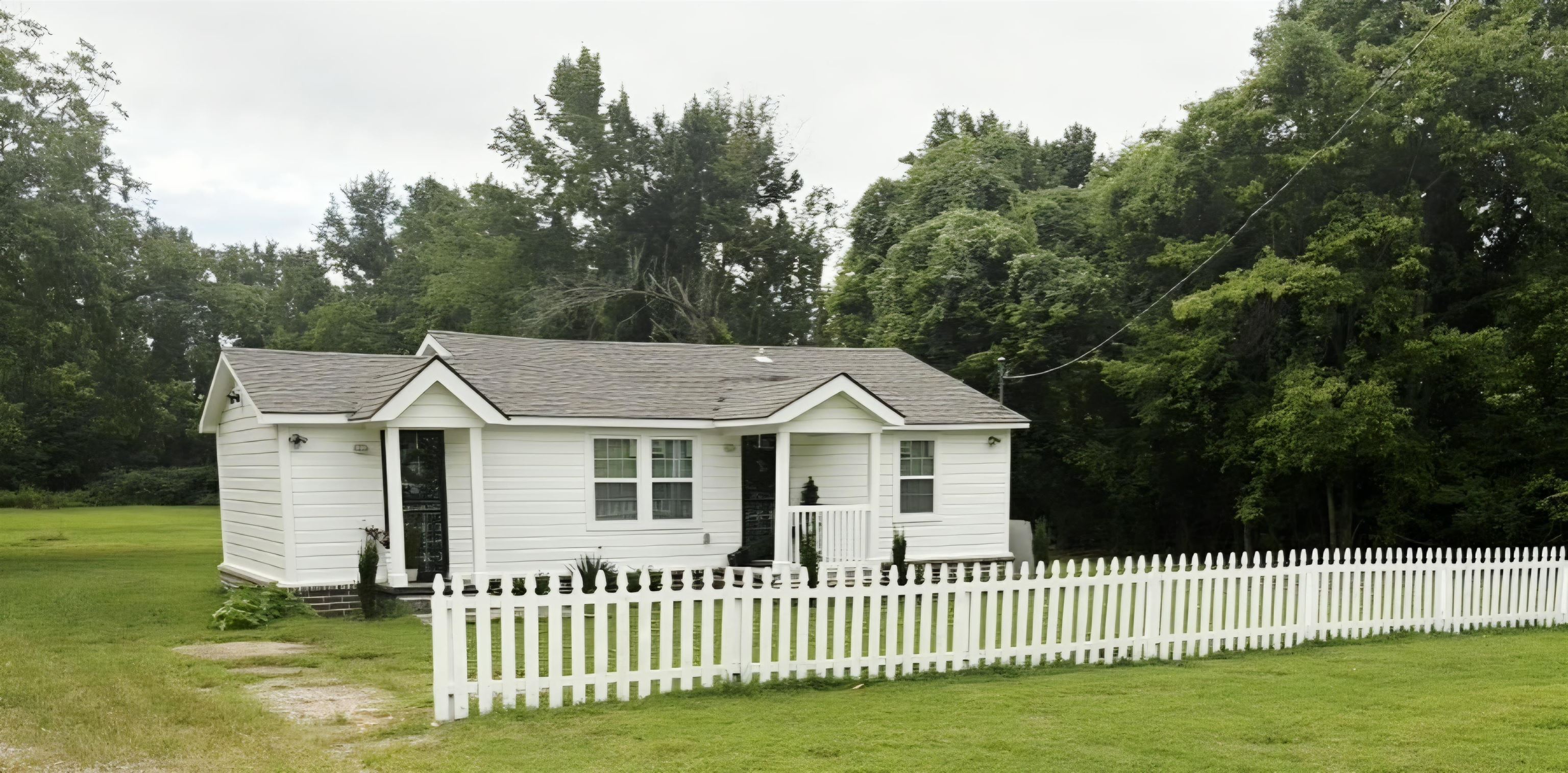 4769 West Union Road Millington, TN 38053 - Photo 1 of 12 White picket fence enclosing a manicured lawn, featuring a white siding exterior with a dark shingle roof, dual covered entryways, and clear window panes