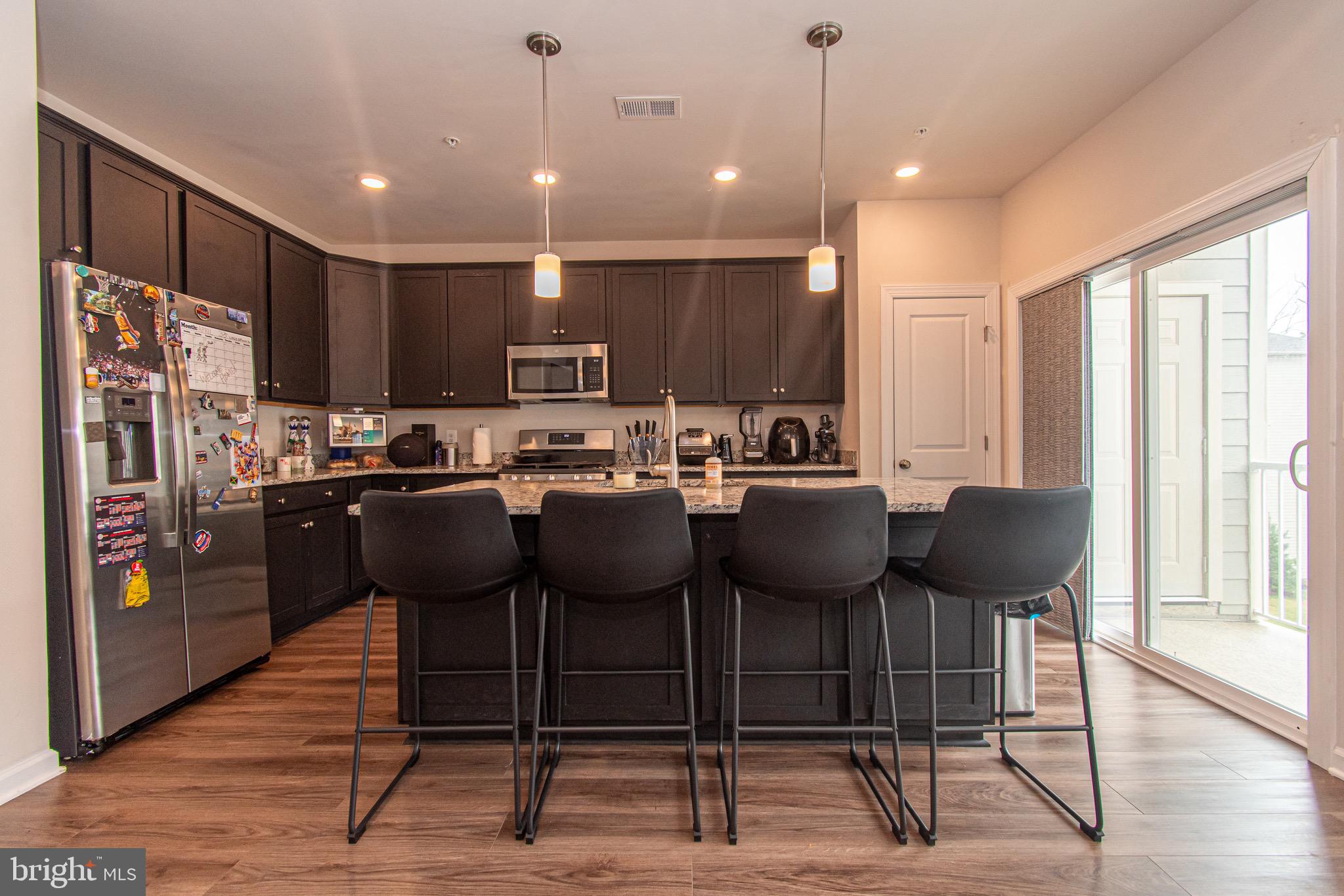 9637 Block Street Lanham, MD 20706 - Photo 16 of 47 a kitchen with stainless steel appliances kitchen island granite countertop a stove a refrigerator a sink a dining table and chairs with wooden floor