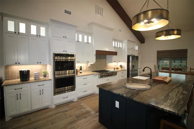 a kitchen with kitchen island granite countertop a stove a sink dishwasher and white cabinets with wooden floor