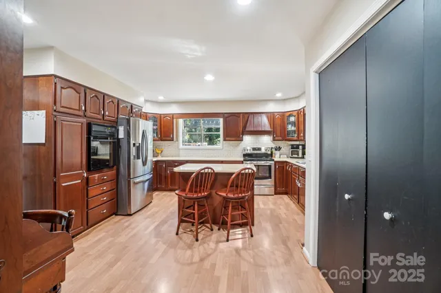 a kitchen with stainless steel appliances granite countertop a refrigerator a sink dishwasher a stove a dining table and chairs with wooden floor