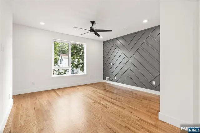 an empty room with wooden floor chandelier fan and windows
