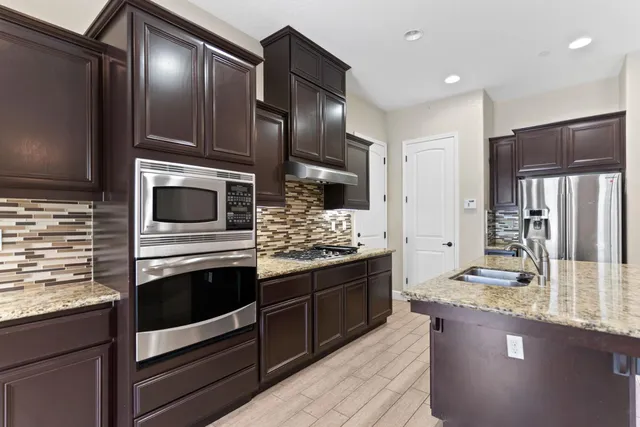 a kitchen with stainless steel appliances kitchen island granite countertop a stove refrigerator and cabinets