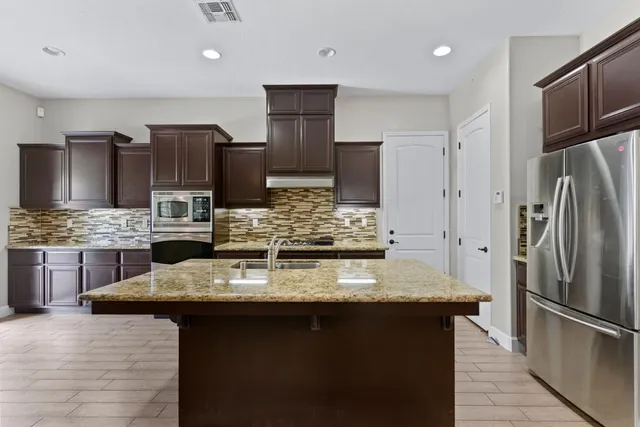 a kitchen with kitchen island granite countertop stainless steel appliances a sink refrigerator and microwave
