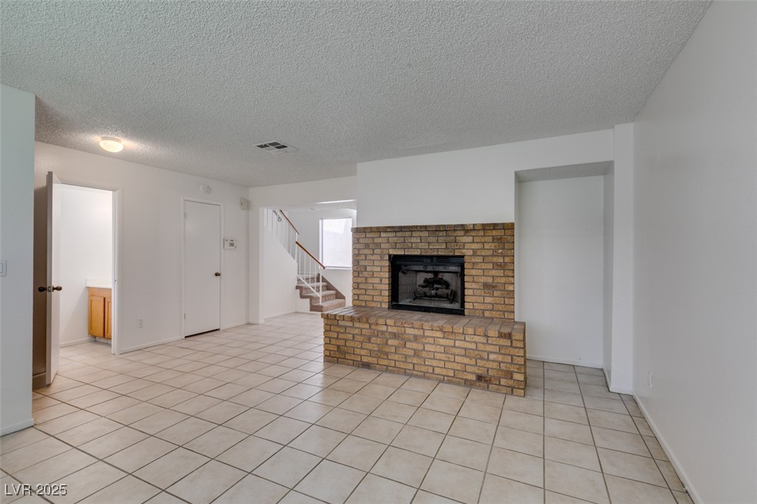 2681 Ruthe Duarte Avenue Las Vegas, NV 89121 - Photo 11 of 43 Unfurnished living room featuring a fireplace, a textured ceiling, visible vents, stairway, and light tile patterned flooring
