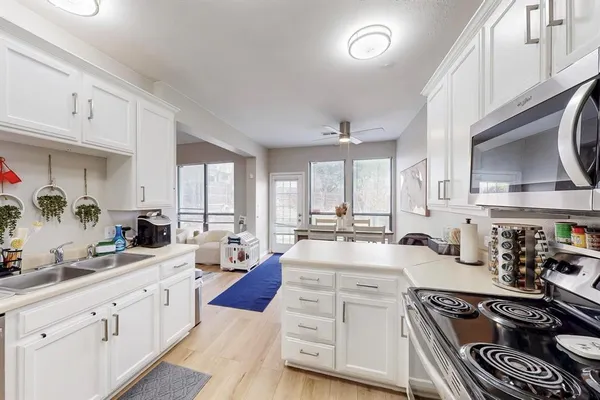 a large white kitchen with stainless steel appliances granite countertop a stove a sink dishwasher and cabinets with wooden floor