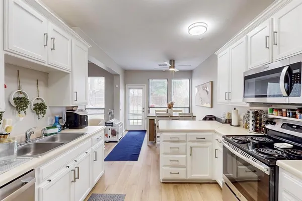 a large kitchen with stainless steel appliances granite countertop a stove a sink dishwasher and white cabinets with wooden floor