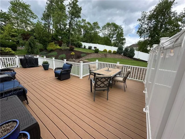 a view of a roof deck with table and chairs couches and a barbeque with wooden fence and floor