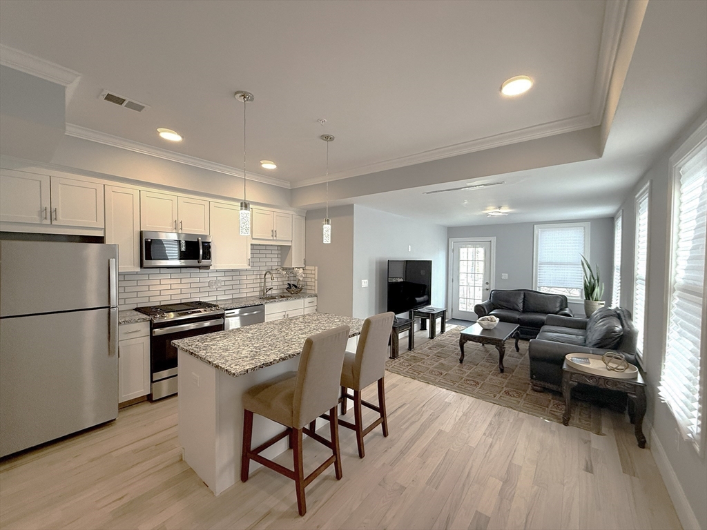7 Waumbeck Street, Unit 3 Boston, MA 02121 - Photo 11 of 21 a kitchen with stainless steel appliances granite countertop a stove a refrigerator a sink a dining table and chairs with wooden floor