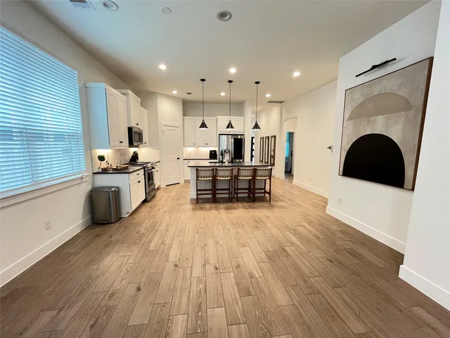 a living room with stainless steel appliances furniture wooden floor and a kitchen view