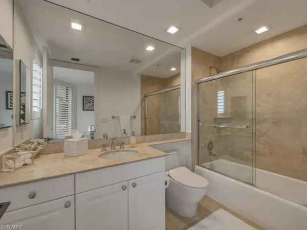 a bathroom with a granite countertop sink a toilet a mirror and a glass door shower