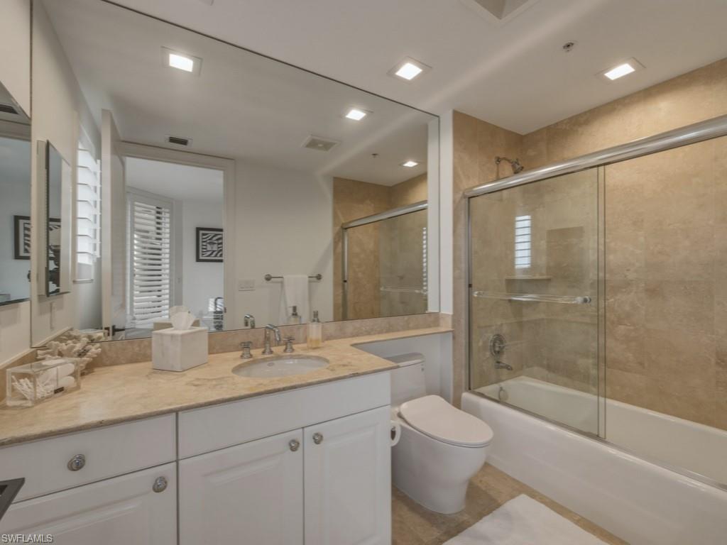 8787 Bay Colony Drive, Unit 306 Naples, FL 34108 - Photo 25 of 40 a bathroom with a granite countertop sink a toilet a mirror and a glass door shower