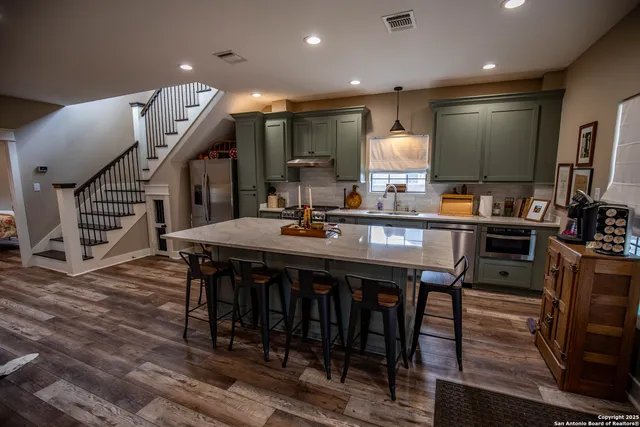 a kitchen with stainless steel appliances granite countertop a refrigerator a stove a sink a dining table and chairs with wooden floor