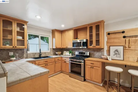 a kitchen with stainless steel appliances granite countertop a stove top oven a sink dishwasher a dining table and chairs with wooden floor